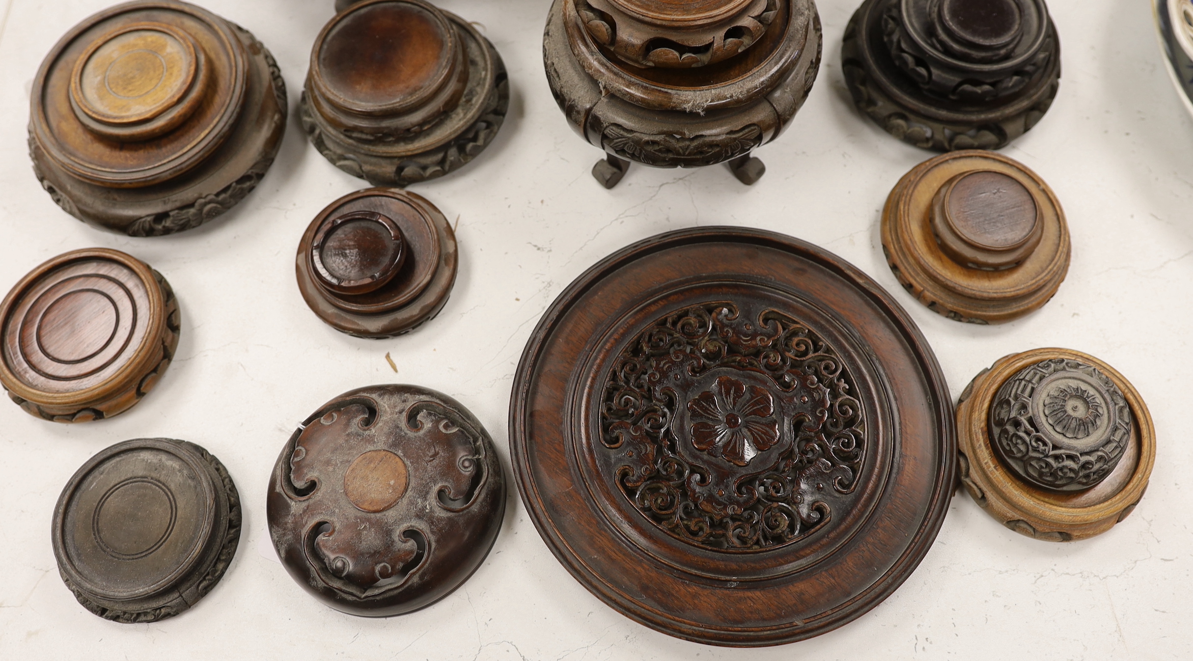 Twenty five assorted Chinese hardwood vase stands and two carved wooden vase covers, largest stand 22cm diameter